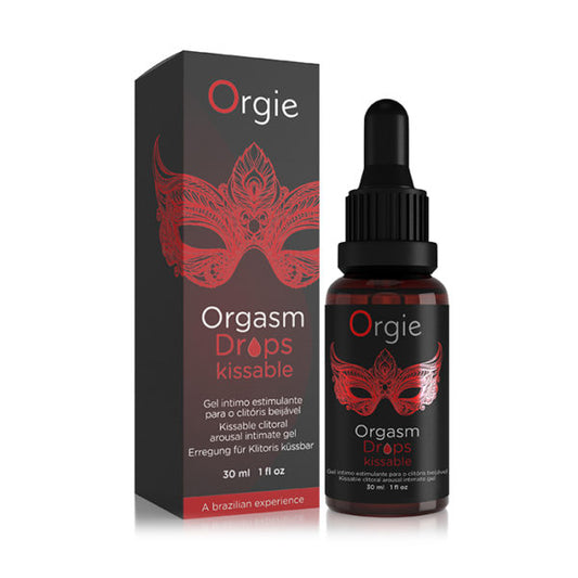 A bottle of Orgie Kissable Orgasm Drops with a red and black label, alongside its black dropper packaging. The packaging features a red mask design and text indicating the product is a 'Liquid Erotic' for enhancing intimate moments.