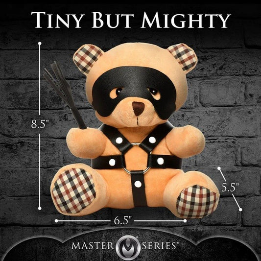 Stuffed toy bear with plaid accents and harness, labeled 'Tiny But Mighty' by Master Series on a dark brick wall background.