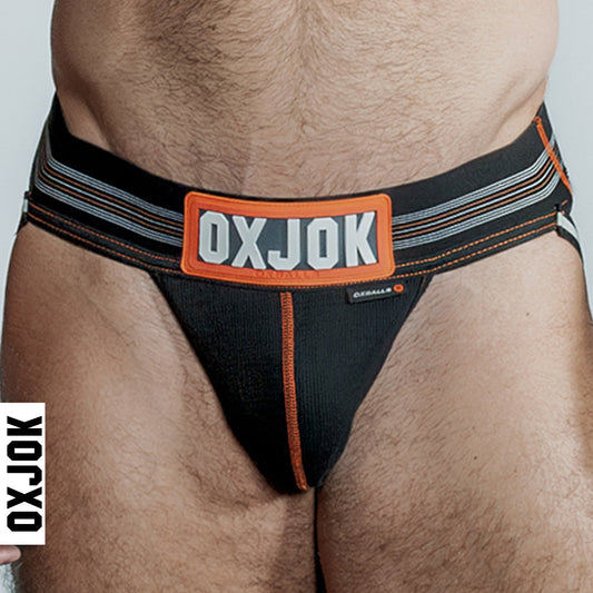 A man wearing a black OXBALLS OXJOK jockstrap, with the brand's logo visible on the waistband.