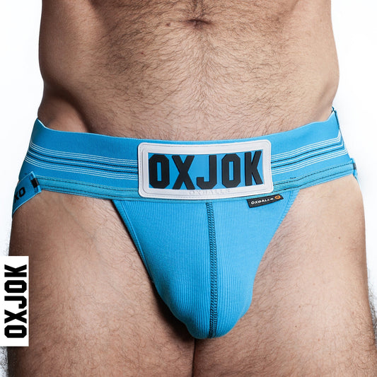 This image features the OXBALLS OXJOK Slingjock, a jockstrap designed for both comfort and visual appeal. The product is presented in a vibrant blue color with a prominent OXJOK branding on the center-front waistband.
