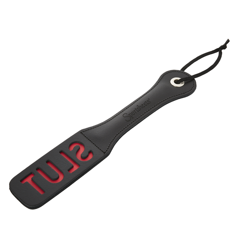 A black leather paddle with the word 'SLUT' printed in red. It has a nickel-free metal tip and a loop for a handle.