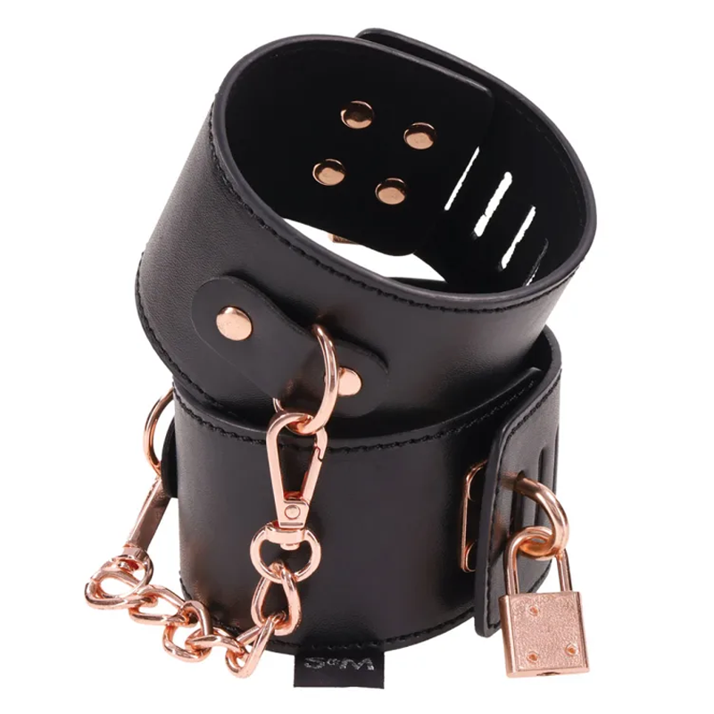 A pair of black cuffs made of vegan leather, featuring rose gold accents. The cuffs are adjustable and have a chain connecting them.