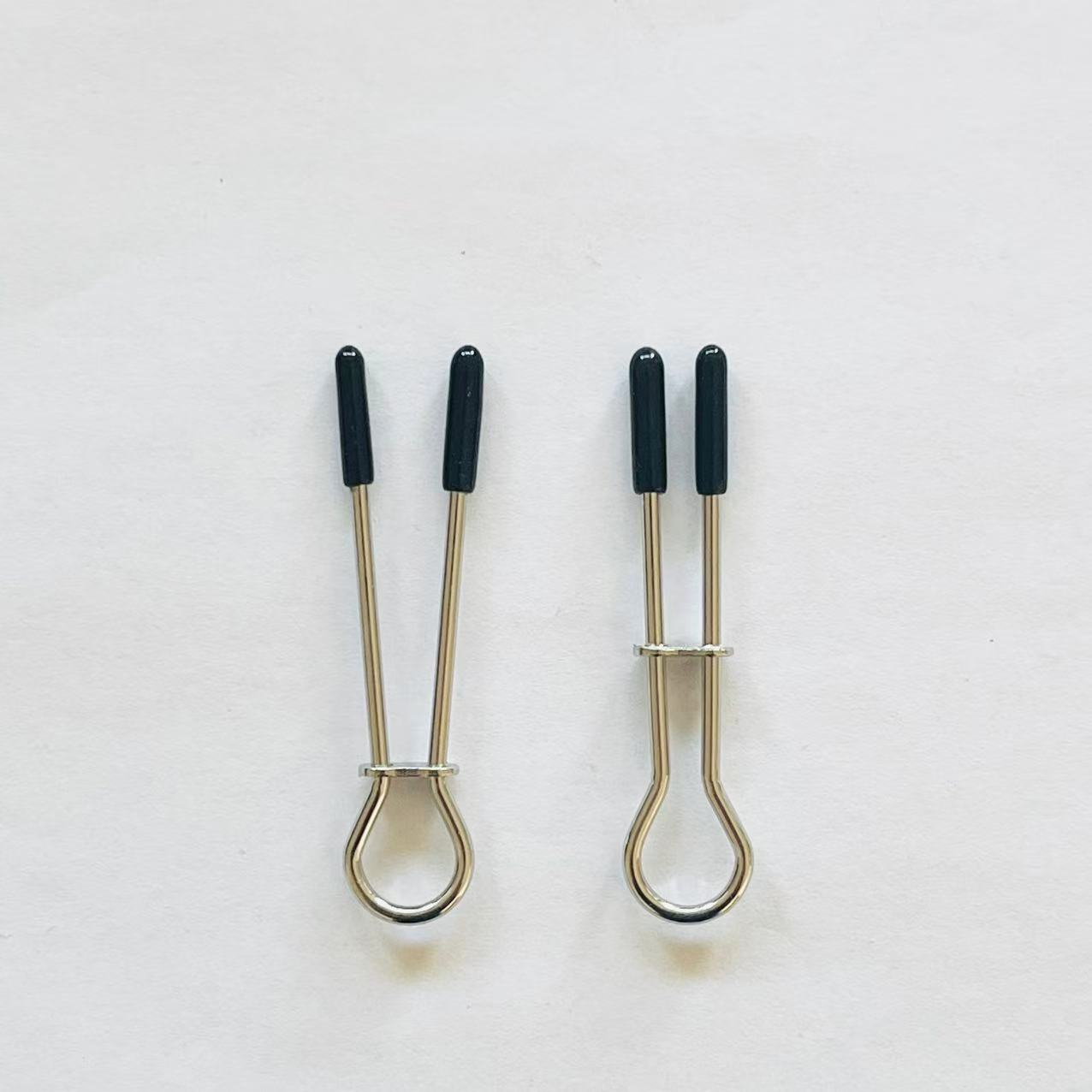 Minimalist stainless steel loop nipple clamps with black rubber tips on white background.
