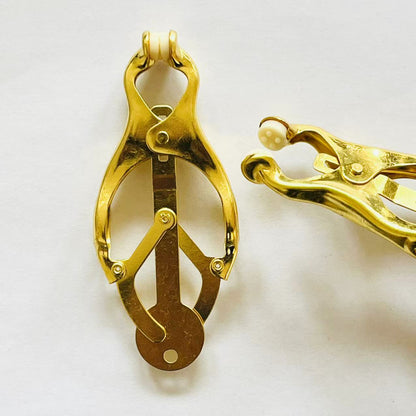 Close-up of gold clover-style BDSM nipple clamps with adjustable tension