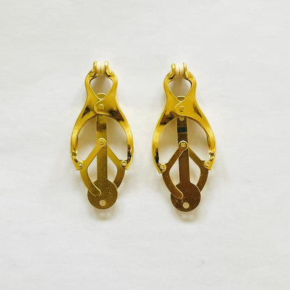 Close-up of gold clover-style BDSM nipple clamps with adjustable tension