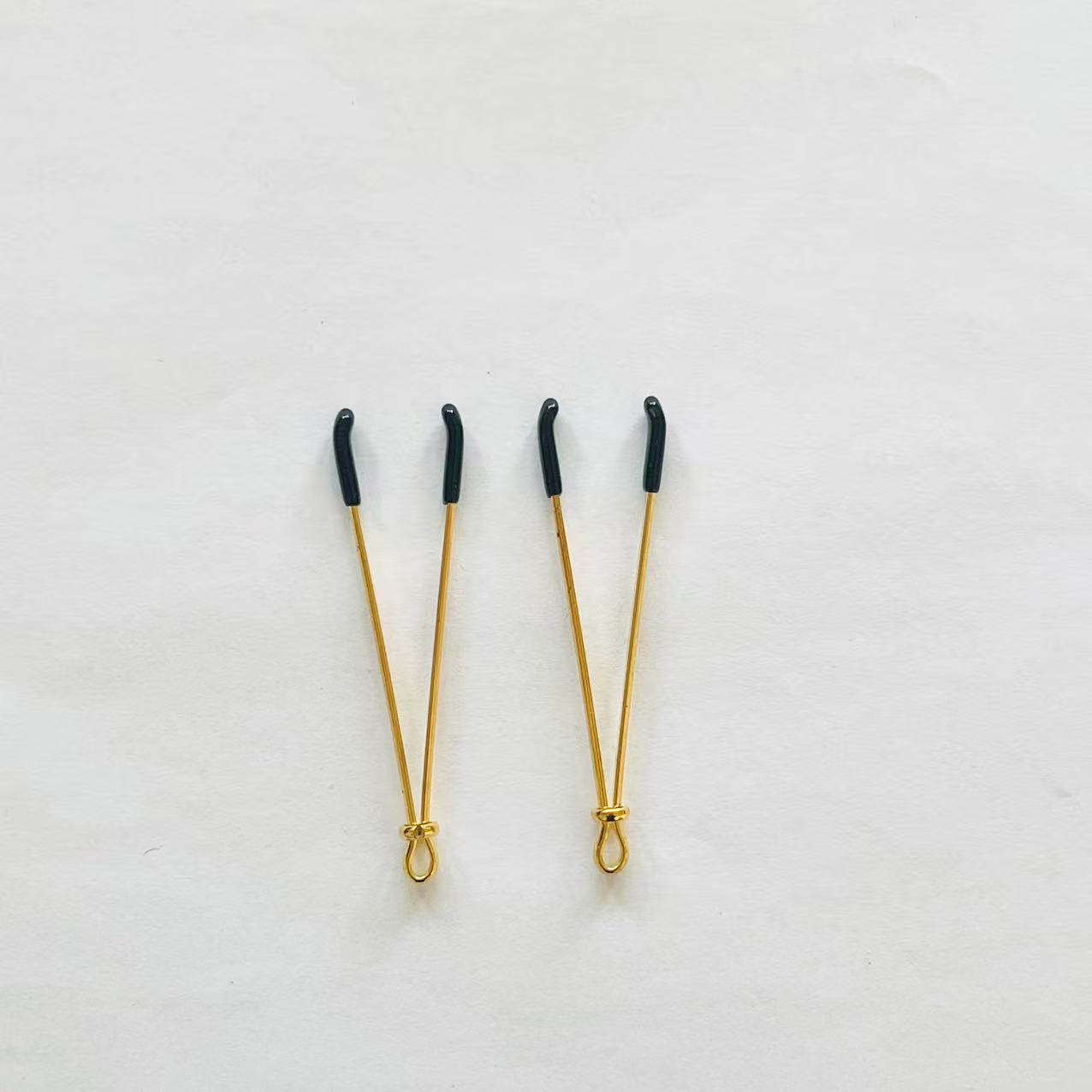 Gold adjustable wire-style nipple clamps with black rubber tips, minimalist BDSM design